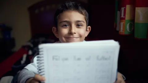 niño sonriendo mostrando un cuaderno hacia la cámara