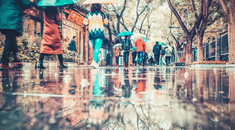 Personas caminando bajo la lluvia en la ciudad con un espejo de agua.