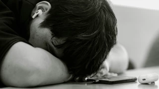 Foto de adolescente recostado sobre mesa con teléfono celular.