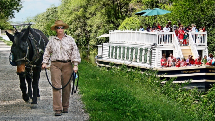 Hombre con un caballo de tiro caminando por el sendero a la vera del río, y una pequeña embarcación con turistas paseando por la zona.