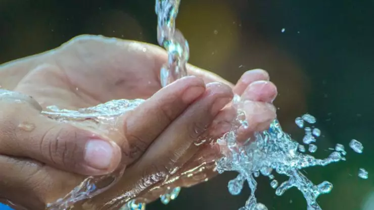 Agua potable cayendo sobre las manos de un joven.