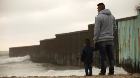 Un hombre y su hijo frente al muro fronterizo que se colocó en la frontera con Tijuana.