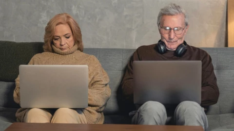 Dos adultos mayores trabajando en una computadora desde su casa