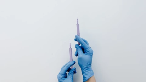 Jeringas sostenidas por unas manos con guantes de médico.