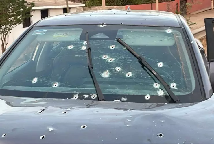 Auto coloro gris oxford con las puertas abiertas y disparos por toda la carrocería y el cristal delantero.