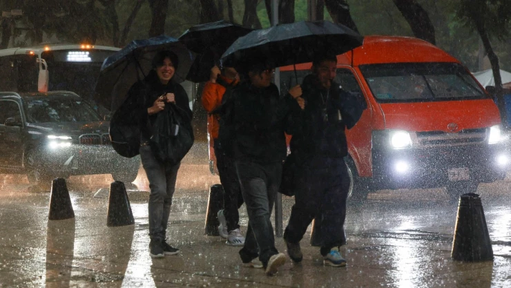 Cuatro personas caminando con paraguas bajo la lluvia en la CDMX.