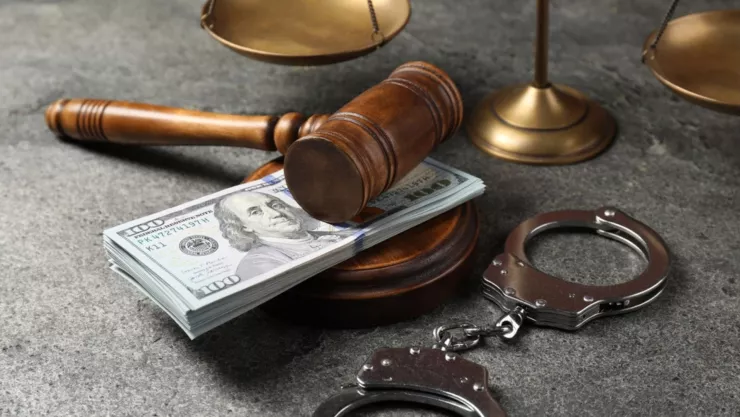Un puñado de billetes de 100 dólares junto a un mazo de un juez y unas esposas.