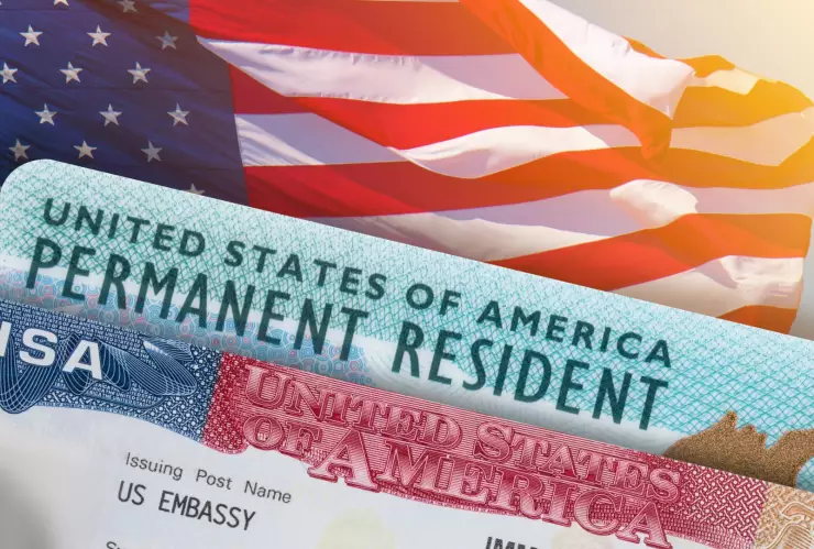 Una Green Card y una visa estadounidense sobre una bandera.