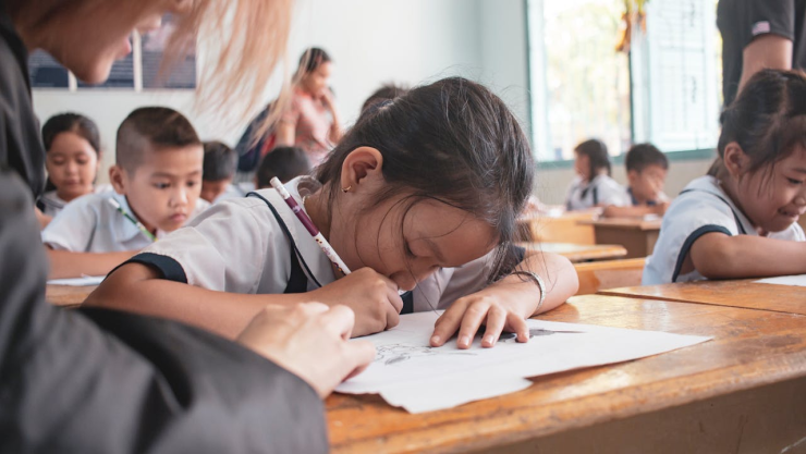 Una alumna escribiendo en su libreta en compañía de su profesora.