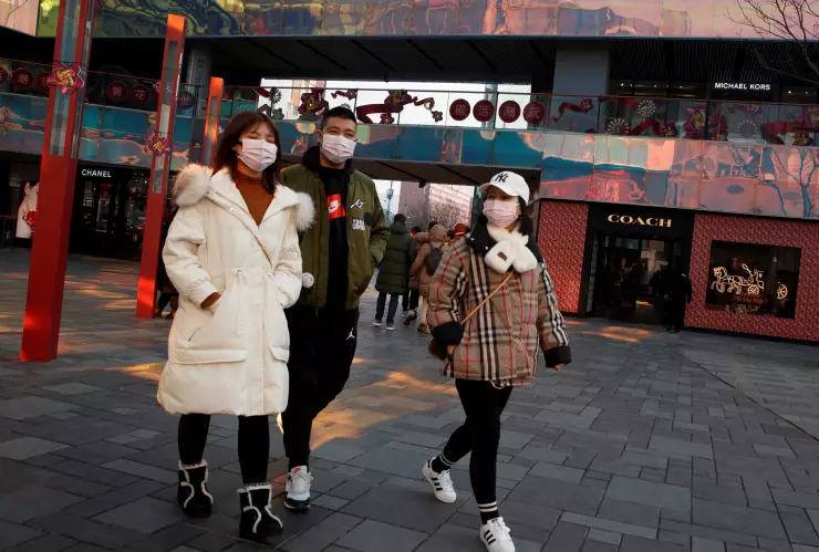 People wearing face masks walk past luxury boutiques in the Sanlitun shopping district in Beijing