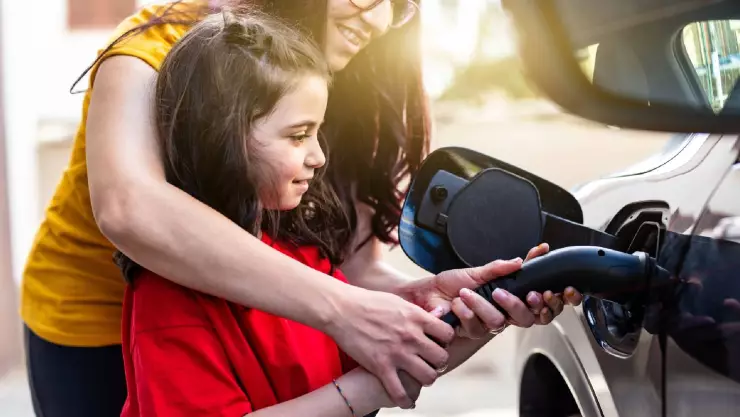 una mujer carga gasolina junto a su niña