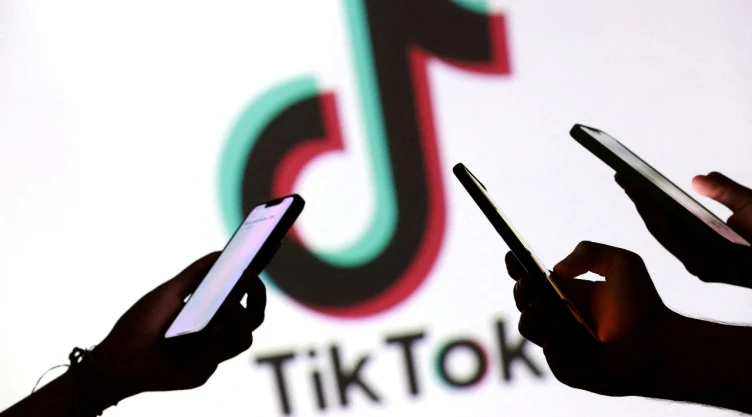 Logo de TikTok detrás de manos con celulares.