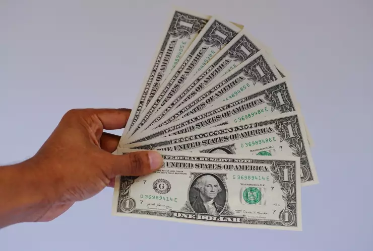 Una mano sostiene varios billetes de un dólar.