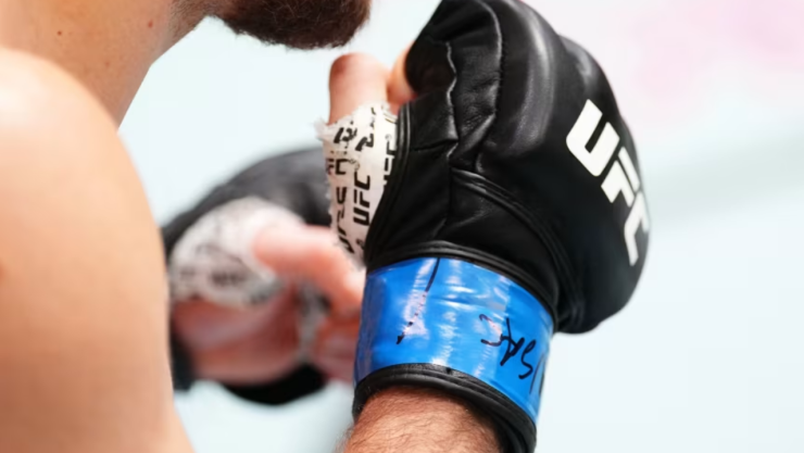 Primer plano de un peleador con guantes negros de UFC y vendas en las manos durante una sesión de entrenamiento de combate.
