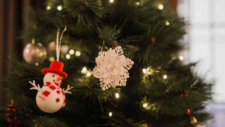 adornos del árbol de navidad, al frente hay un hombre de nieve con un sombrero rojo y una bufanda con detalles blancos, también hay un ornamento de copo de nieve, además de luces y esferas