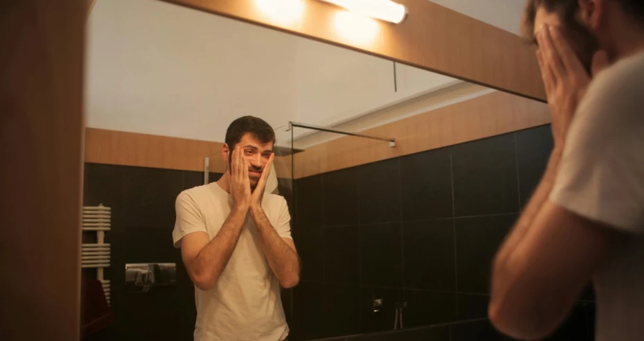 Hombre de cabello corto frente al espejo con rostro cansado