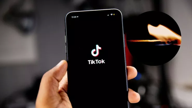 Imagen de mano sosteniendo celular con pantalla de tiktok y cerillo encendido con flama.