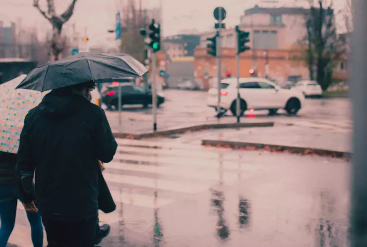 Personas caminando bajo la lluvia en la ciudad con paraguas en mano.
