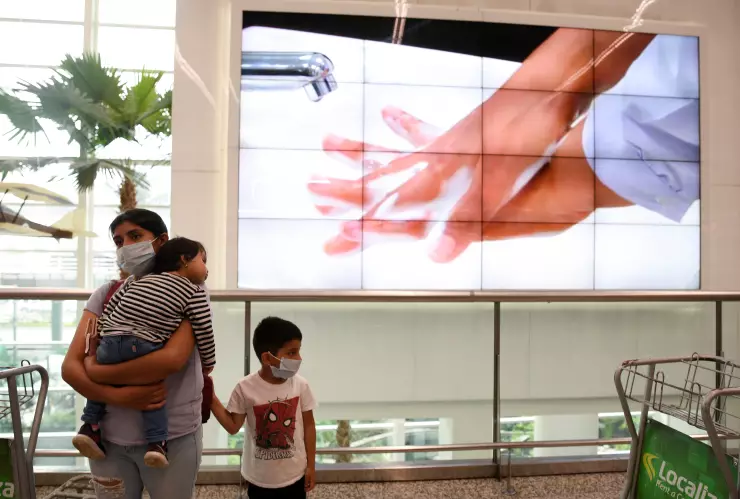 Una mujer y su hijo usan mascarillas cerca de una pantalla que muestra los pasos para lavarse las manos, como parte de las medidas de seguridad debido al brote del coronavirus (COVID-19), en el Aeropuerto Internacional José Joaquín de Olmedo en Guayaquil
