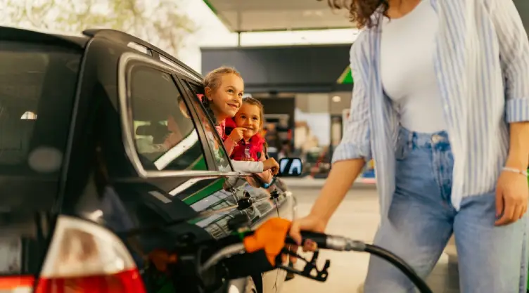 una madre carga combustible mientras observa a sus pequeñas niñas