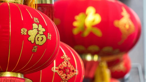 Primer plano de linternas chinas rojas con detalles dorados y una de ellas tiene un caracter que simboliza buena fortuna, colgadas como decoración festiva.