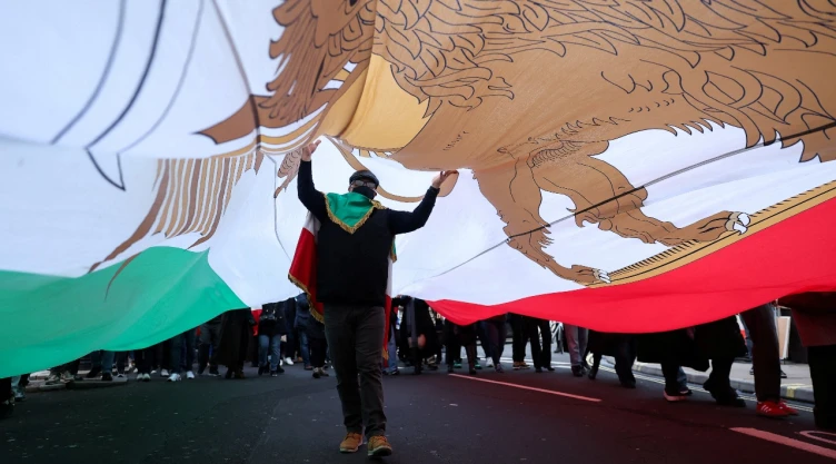 Persona camina con bandera de Irán encima en protesta en Londres, Inglaterra.