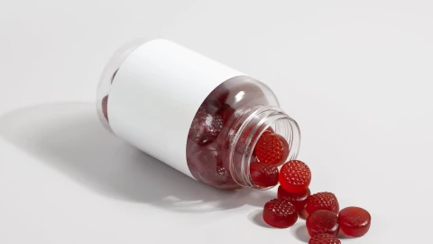 Gomitas de color rojo salen de un frasco de medicamentos.