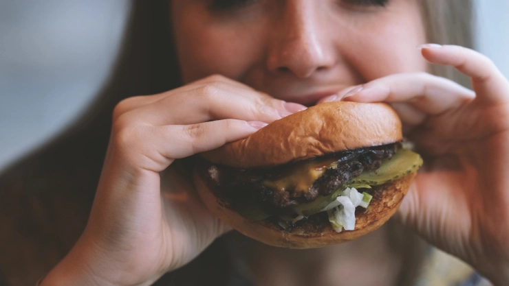 Mujer come hamburguesa en restaurant de comida rápida