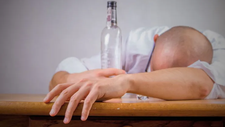 Un hombre con camisa blanca borracho sosteniendo una botella en su mano