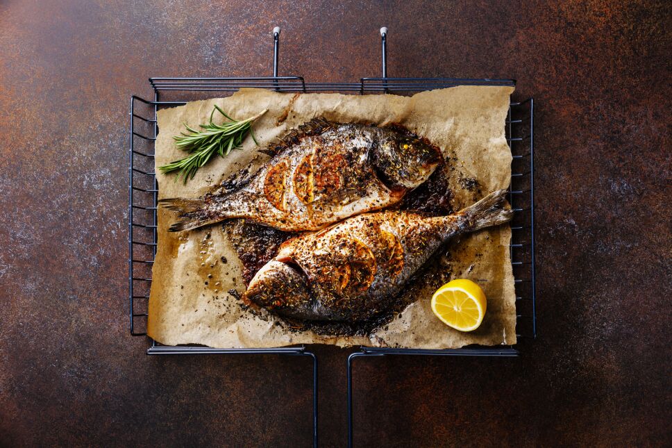 Grilled Fish Dorado on metal grill grid with lemon and rosemary