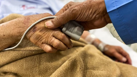 La mano de un paciente internado en un hospital sostenida por la mano de uno de sus familiares.