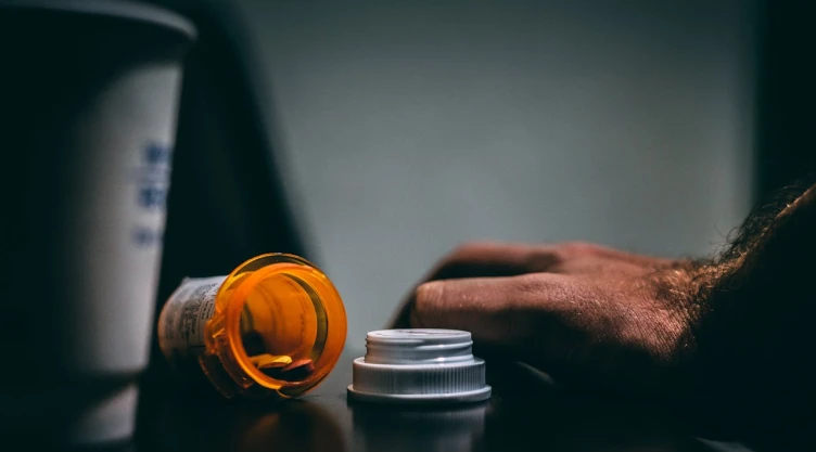 Frasco de medicamentos color naranja con tonos oscuros y una mano.