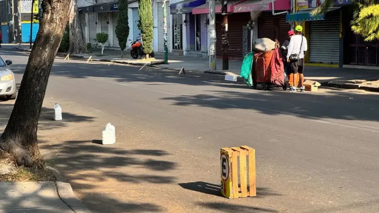 Franeleros en CDMX apartando lugar con botes en la calle.