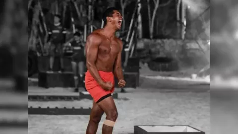 Atleta sin playera con short rojo gritando durante una competencia en la playa