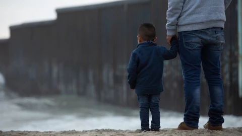 Un niño de la mano de su papá en la valla fronteriza de Estados Unidos.