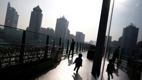 Una ni&ntilde;a pasa corriendo junto a un hombre mientras &eacute;ste fuma en el &aacute;rea central de negocios de Pek&iacute;n