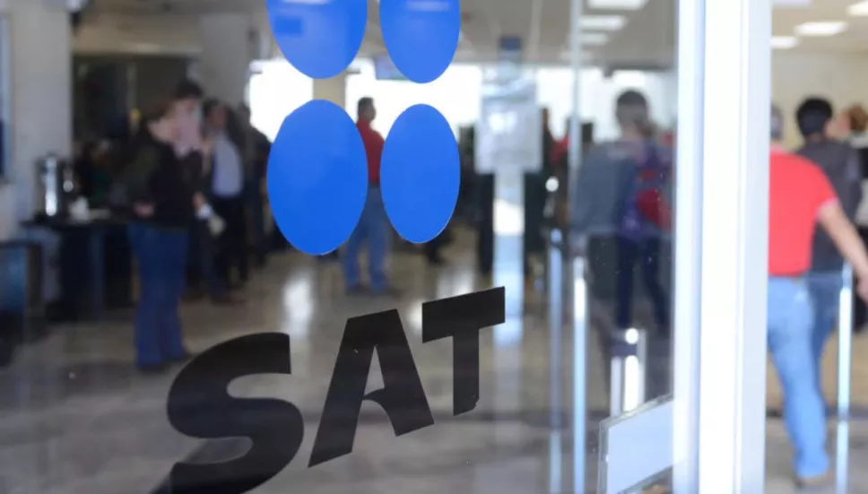 Puerta de cristal en las oficinas del SAT con el logo de la institución, en el fondo se ven varias personas