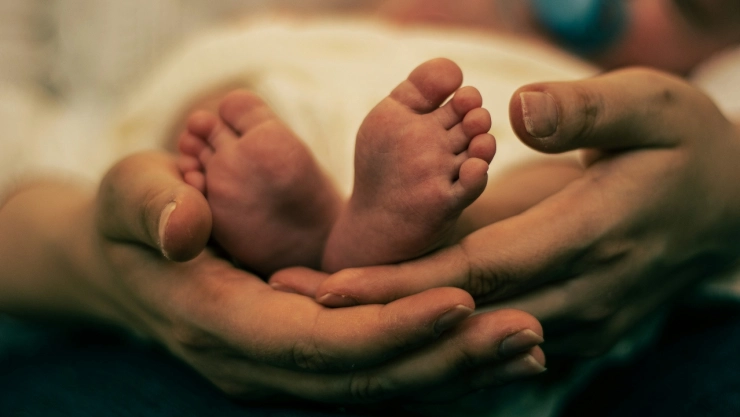 Pies de bebé sujetados por manos de adulto.