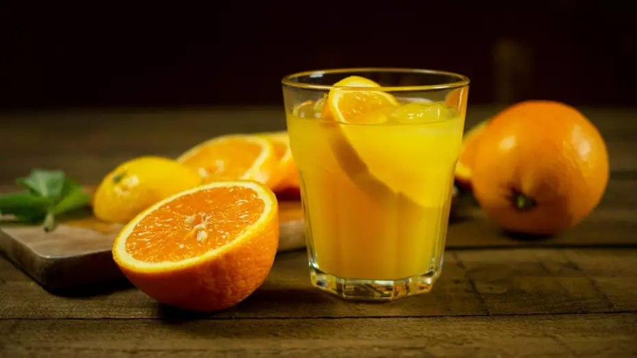 vaso de jugo con naranjas alrededor.