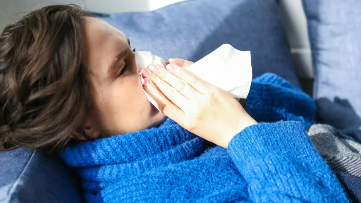Una mujer con un suéter azul enferma de gripe solar sonándose la nariz