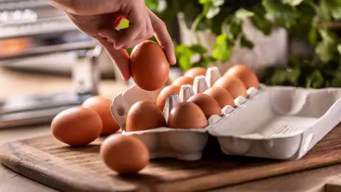 Una mujer agarra un huevo de la caja de cart&oacute;n