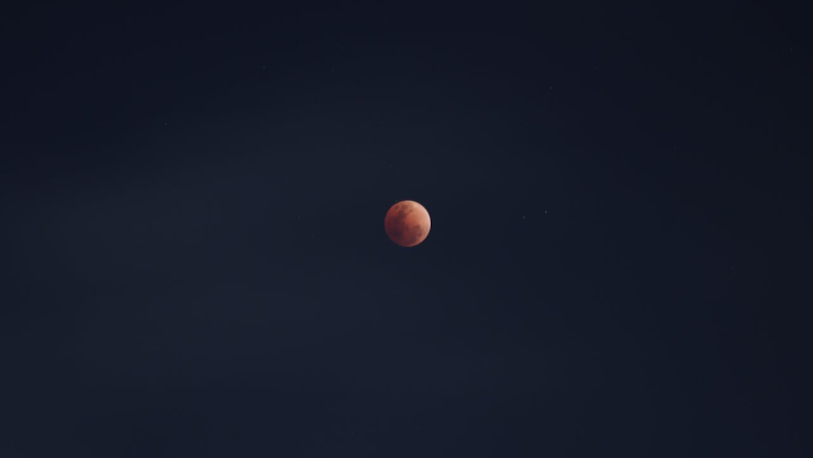 En el cielo nocturno, la Luna se alza teñida de un rojo profundo, como si ardiera suavemente en la oscuridad durante el eclipse solar.