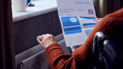 Una mujer revisa la factura de energía al lado de la calefacción.