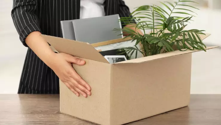 una mujer con caja de pertenencias personales en la mesa de una oficina