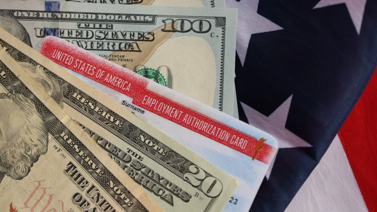 Una tarjeta de autorización de empleo estadounidense y billetes de dólares.