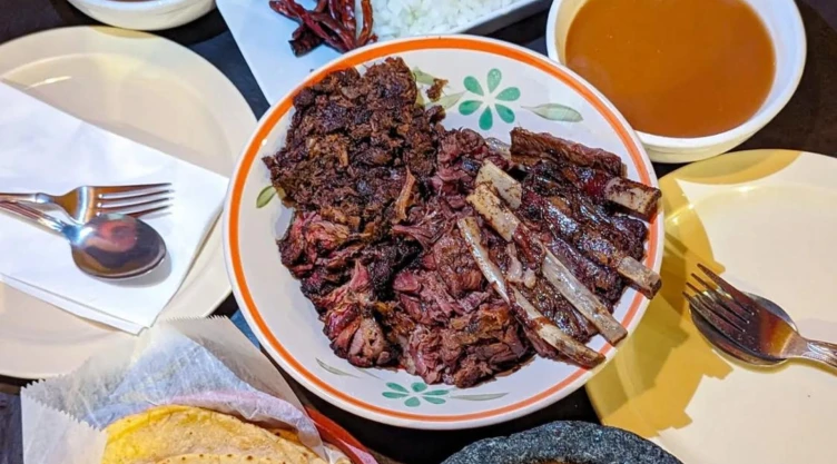 Plato de carne de chivo con sus pequeñas costillas, acompañadas de salsas mexicanas y los cubiertos