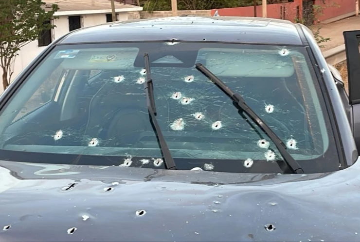 Auto coloro gris oxford con las puertas abiertas y disparos por toda la carrocería y el cristal delantero.