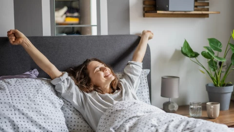 Una mujer se estira sonriente en su cama.