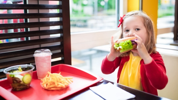 Niña come una hamburguesa en shopping