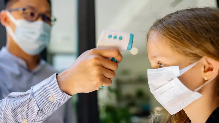 Hombre tomándole la temperatura a una niña con pistola de termómetro y cubrebocas.